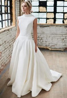 a woman in a white wedding dress is standing by a brick wall and looking off into the distance