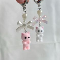 a person holding two key chains with small charms attached to them, one is pink and the other is white