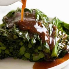 someone is pouring sauce on top of some green veggies in a white plate