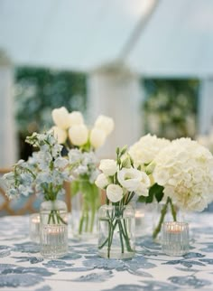 three vases filled with white flowers sitting on top of a blue table cloth covered table