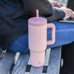 a person sitting on a bench with a laptop and pink cup in front of them