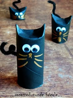 three black cat made out of toilet paper on top of a wooden table with googly eyes