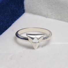 a white gold ring with a triangular shaped diamond in the center on a blue and white background