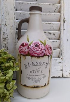 a white jug with pink roses painted on it sitting next to a potted plant