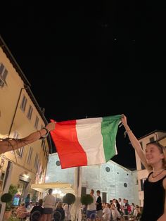 a man and woman holding an italian flag in front of a building at night time