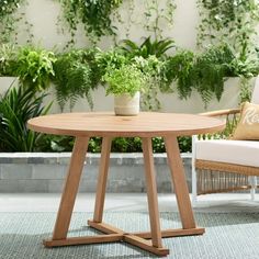 a wooden table sitting on top of a rug next to a white chair and potted plant