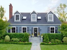 a blue house with white trim and windows in the front yard is surrounded by greenery