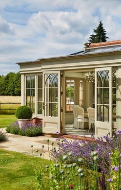 an orangery with glass doors and windows on the side, surrounded by purple flowers