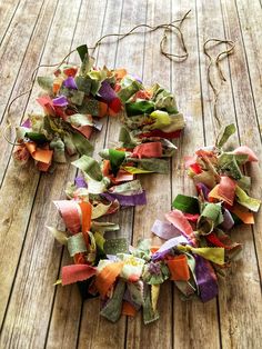 a wreath made out of colorful fabric on a wooden floor with string and scissors in the background