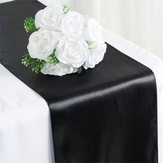 a black table runner with white flowers and greenery on the top is ready to be used as a centerpiece