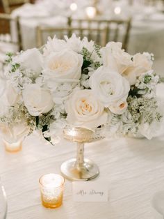 a vase filled with white flowers sitting on top of a table next to two candles