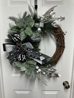 a wreath on the front door decorated with silver, black and white decorations for christmas