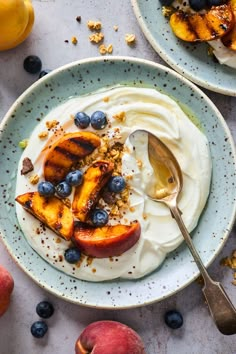 two plates with yogurt and fruit on them, next to peaches and blueberries