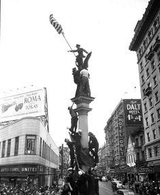 an old black and white photo of a statue in the middle of a crowded street