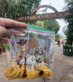 someone is holding up a plastic bag with toy characters inside it in front of a sign that reads dinoland usa