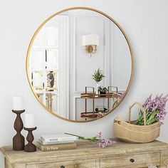 a mirror on the wall next to a dresser with flowers and a basket sitting on it