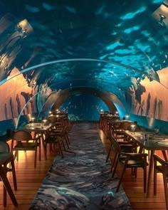 the inside of a restaurant with tables and chairs under an underwater tunnel that is lit up