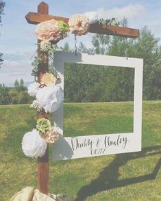 a wedding photo frame with flowers and greenery hanging from it's side in the grass