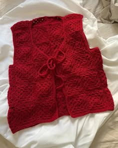 a red knitted cardigan laying on top of a bed next to a pillow