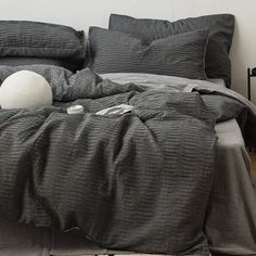 an unmade bed with dark gray linens and pillows on the bottom, along with a white ball