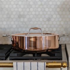 a copper pan sitting on top of a stove next to a white and gold towel