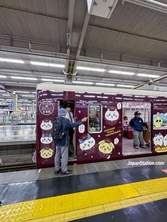 two people standing on the platform next to a train with cartoon characters painted on it