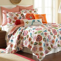 a bed covered in lots of colorful pillows and blankets on top of a wooden floor