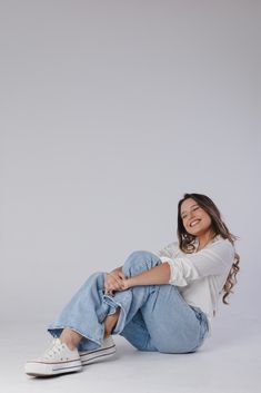 a woman sitting on the ground with her legs crossed and smiling at the camera,