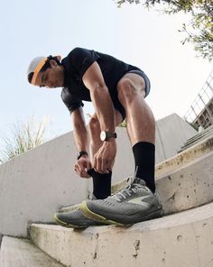 a man in black shirt and shorts tying his shoelaces on concrete step next to cement wall