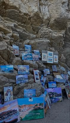 many paintings are displayed on the side of a cliff near some water and rocks,