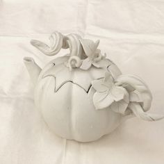 a white ceramic teapot with flowers on it's side sitting on a table