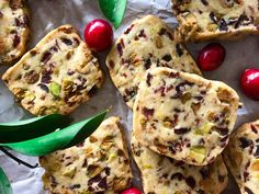 cookies with cranberries and nuts are arranged on wax paper next to green leaves