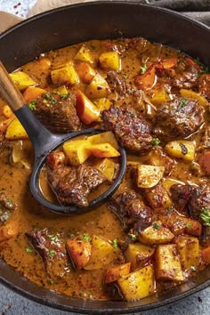 a pot filled with stew and potatoes on top of a table next to a wooden spoon