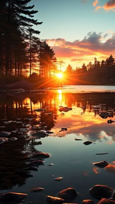 the sun is setting over a lake with rocks in front of it and trees on both sides