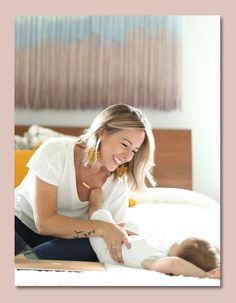 a woman holding a baby while sitting on top of a bed