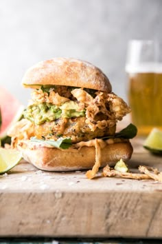 a chicken sandwich with lettuce, avocado and salsa on a wooden cutting board