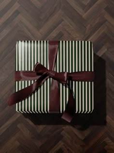 a present wrapped in brown and white striped paper with a red bow on it sitting on a wooden floor