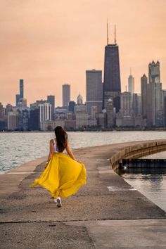 a woman in a yellow dress is walking by the water with her back to the camera