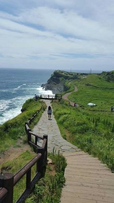 a person is walking down a path near the ocean and grassy area with benches on it