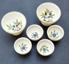 six small bowls with blue berries and green leaves painted on the bottom one is empty