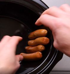 three hot dogs in a black bowl being held by someone's hands over it