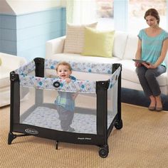 a baby in a playpen with a woman sitting on the couch behind it and looking at him