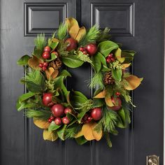 a christmas wreath on the front door with pine cones, berries and evergreen leaves hanging from it