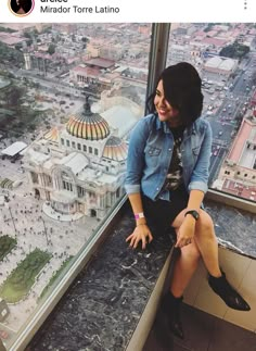 a woman sitting on top of a window sill looking out at the city below