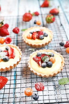 three small tarts with fruit on top of them sitting on a cooling rack next to some strawberries and raspberries