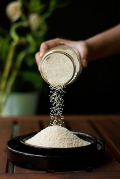 someone pouring rice into a black bowl on top of a wooden table with flowers in the background