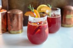 three glasses filled with red liquid and garnished with oranges, lemons and rosemary