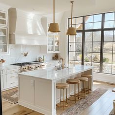 a large kitchen with white cabinets and marble counter tops, gold pendant lights over the island