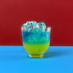 a glass filled with liquid and ice on top of a blue table next to a red wall