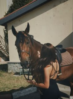 a woman standing next to a brown horse in front of a white building with stairs